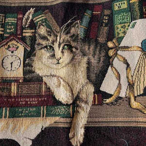 May include: Tapestry depicting a tabby cat amidst a library setting. The cat has green eyes and is positioned near a clock and books. The colour scheme includes browns, greens, and burgundy, creating a cosy, literary atmosphere.