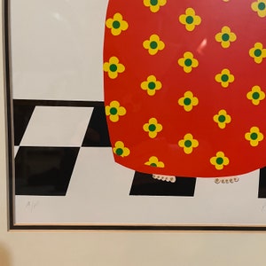 May include: A red dress with a yellow and green floral pattern. The dress is worn by a person standing on a black and white checkered floor. The image is signed "A/P".