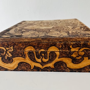 May include: A wooden box with intricate carvings. The box features a dark brown exterior with lighter brown carved floral and scroll designs. The top and sides are adorned with detailed patterns, creating a decorative storage piece.