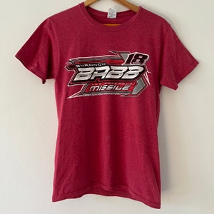 May include: Red t-shirt with a white graphic of a race car with the text "Shannon Babb The Monstrous Missile" and the number "18".