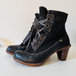 Könnte beinhalten: Ein Paar schwarze Leder- und Wildlederstiefeletten mit braunen Schnürsenkeln und einem Blockabsatz. Die Stiefel haben eine runde Spitze und sind mit hellbraunem Faden genäht. Der Absatz ist ca. 7,6 cm hoch.