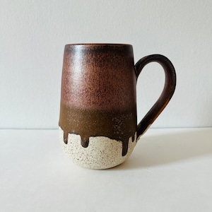 Può includere: Una tazza in ceramica marrone e bianca con una glassa macchiata. La tazza ha un corpo arrotondato e un manico.