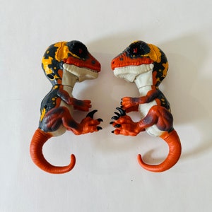 May include: Two black, orange, and yellow dinosaur toys with red eyes. The dinosaurs are facing each other and have their mouths open.