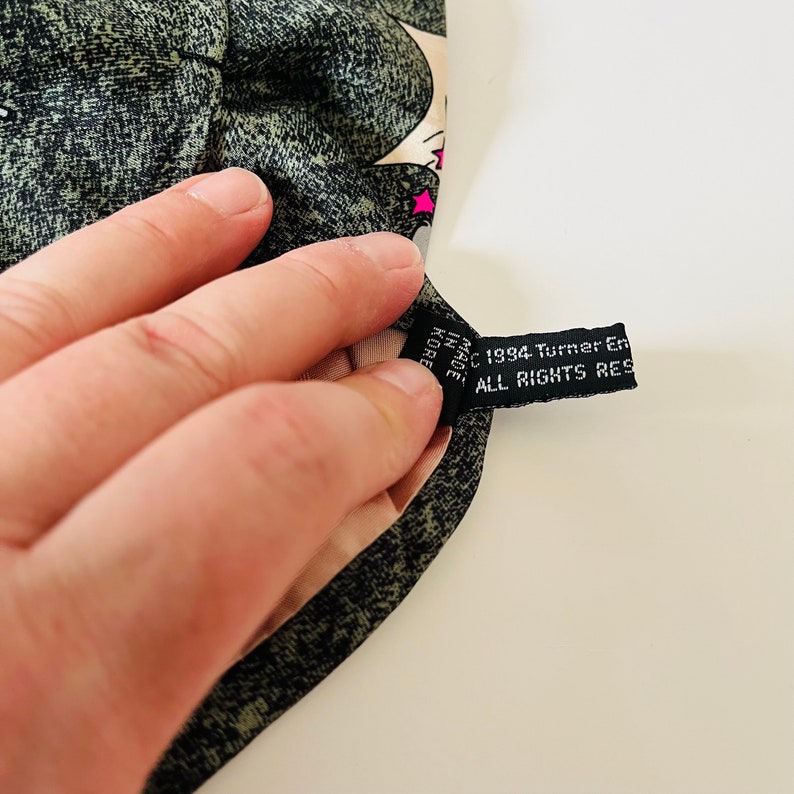 May include: A black fabric tag with white text that reads "&copy; 1984 Turner Entertainment Co. ALL RIGHTS RESERVED" and "MADE IN KOREA".