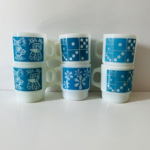 May include: Six vintage milk glass mugs with blue and white designs. Two mugs feature a chair and rocking chair design, two mugs feature a domino design, and two mugs feature a floral design.