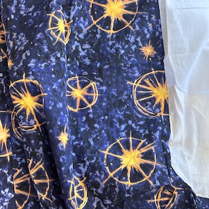 May include: A navy blue fabric with a pattern of yellow starbursts and white speckles. The fabric is folded, revealing a section of plain white fabric on the right side. The starbursts have a sun-like design.