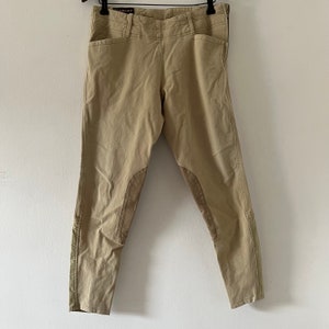 Könnte beinhalten: Eine beige Reithose mit Leder-Kniepolstern. Die Hose hat einen Reißverschluss und Gürtelschlaufen.