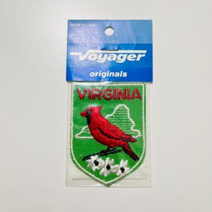 May include: Embroidered patch featuring a red cardinal perched on a branch with white flowers, set against a green shield with the word "VIRGINIA" and a state outline. The patch is packaged with a blue Voyager Originals header.