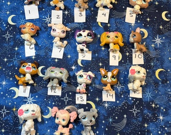 May include: A collection of 18 small plastic pet toys, each with a different design and color. The toys are arranged in rows on a blue and white patterned fabric.
