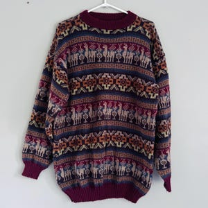 Peut inclure: Un pull en tricot à manches longues présentant un motif répétitif de lamas et de formes géométriques dans des tons bordeaux, bleu marine, beige et crème. Le vêtement possède un col rond, des poignets et un ourlet côtelés en bordeaux uni.