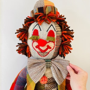 May include: A vintage patchwork clown doll with a red nose, brown yarn hair, and a bow tie. The doll is made of fabric and has a whimsical expression.