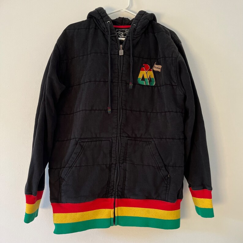 May include: Black quilted zip-up hoodie with a red, yellow, and green striped band at the bottom and a green, yellow, and red patch on the front with the text "Habibi".