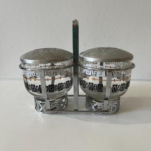 Könnte beinhalten: Ein Set aus zwei silberfarbenen Glasschalen mit schwarzen und goldenen geometrischen Mustern. Die Schalen stehen auf einem passenden silberfarbenen Ständer mit Griff.