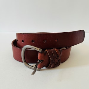 May include: A brown leather belt with a braided design and a silver buckle. The belt is folded in half and the buckle is visible.