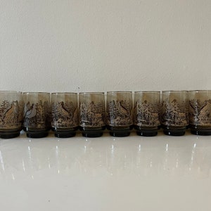 May include: Set of eight brown glass tumblers with a black and white bird design. The glasses have a rounded bottom and a straight side.