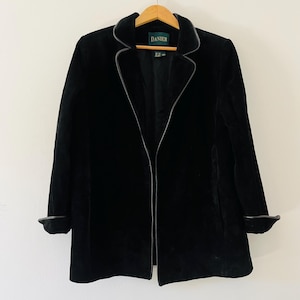 May include: Black velvet blazer with a white trim around the collar and cuffs. The blazer has a zip fastening and the label "DANIER" is visible on the front.