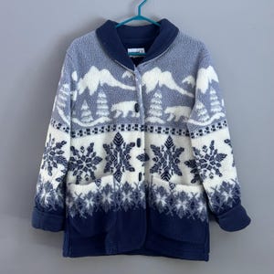 May include: A blue and white fleece jacket with a snowflake and bear pattern. The jacket has a button closure and two pockets.