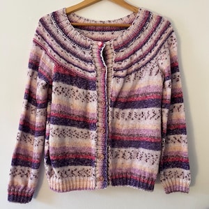 May include: A striped cardigan with a pink button closure. The cardigan is made of a soft, knitted fabric and features a variety of colors, including pink, purple, and white.