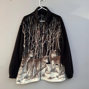 May include: Black fleece jacket with a full-zip fastening. The jacket features a forest scene with wolves and bare trees in shades of brown and white. The sleeves are solid black.