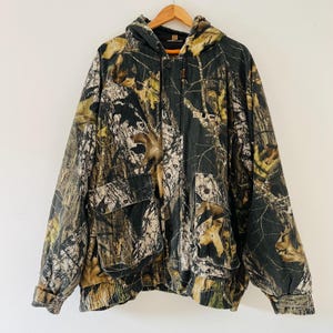 May include: A green, brown, and tan camouflage hooded jacket with a button closure and the word "BUCK" on the front.