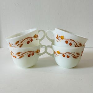 May include: Set of six white milk glass teacups with a floral and wheat design in shades of orange and yellow.