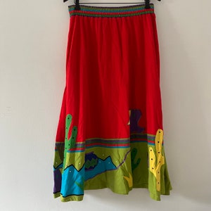May include: A red maxi skirt with a green, blue, and yellow southwestern-inspired print. The skirt has a wide elastic waistband and a flowing silhouette.