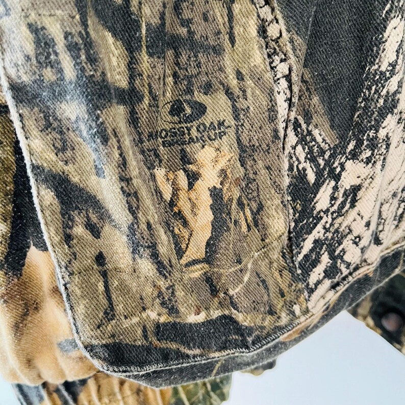 May include: Close-up of a camouflage fabric with the words "Mossy Oak Break-Up" printed on it.