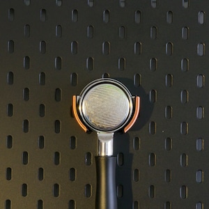 Peut inclure: Un porte-filtre à café en argent avec une bordure de couleur cuivre et une poignée noire. Le porte-filtre est conçu pour être utilisé avec une machine à espresso.