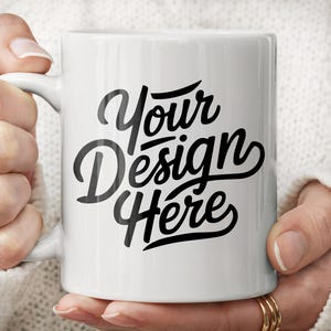 Peut inclure: Une tasse en c&eacute;ramique blanche avec un motif noir qui dit "Your Design Here" dans une police stylis&eacute;e.