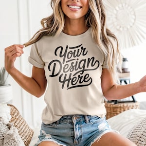 May include: A beige t-shirt with rolled-up sleeves featuring the text "Your Design Here" in a black, cursive font. The model is wearing denim shorts. The shirt is a blank canvas for custom designs.