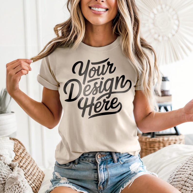 May include: A beige t-shirt with rolled-up sleeves featuring the text "Your Design Here" in a black, cursive font. The model is wearing denim shorts. The shirt is a blank canvas for custom designs.