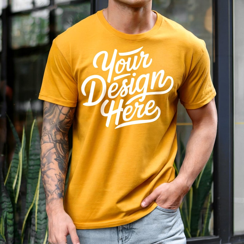 K&ouml;nnte beinhalten: Ein senfgelbes T-Shirt mit dem Text "Your Design Here" in wei&szlig;en Buchstaben.