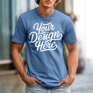 May include: A light blue t-shirt with the text "Your Design Here" in white script. The short-sleeved shirt is made of a soft material and is being modeled.