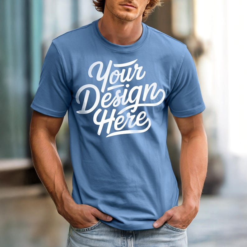 May include: A light blue t-shirt with the text "Your Design Here" in white script. The short-sleeved shirt is made of a soft material and is being modeled.