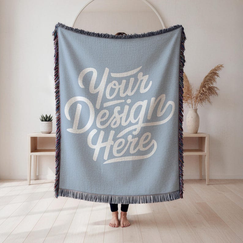 May include: A light blue woven throw blanket with the text "Your Design Here" in white script. The blanket has a fringed edge with a mix of colors. The blanket is displayed indoors.