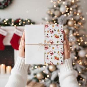 Puede incluir: Un regalo envuelto con un diseño navideño blanco y estampado. El lado estampado presenta a Papá Noel, muñecos de nieve y hombres de jengibre. El regalo está atado con hilo y se sostiene frente a un árbol de Navidad y una chimenea.