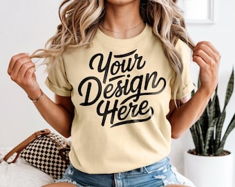 May include: A light yellow t-shirt with rolled sleeves featuring the text "Your Design Here" in a bold, black script. The model is wearing denim shorts and a gold necklace. The shirt is a casual, everyday wear item.