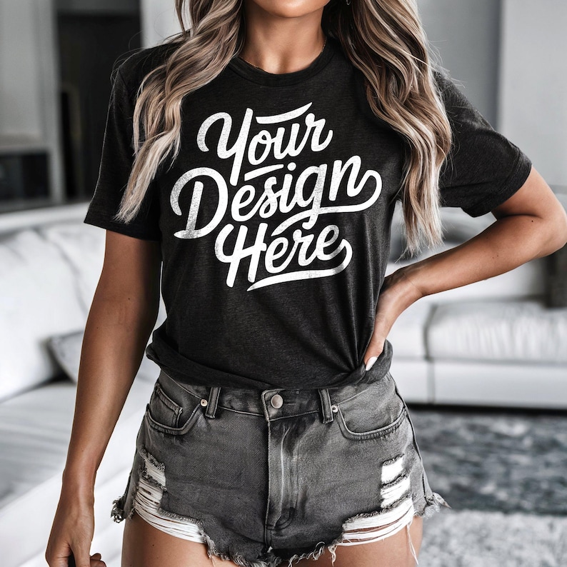 Peut inclure: Un t-shirt noir avec le texte "Your Design Here" en lettres blanches. Le t-shirt est port&eacute; par une personne aux cheveux blonds longs et est associ&eacute; &agrave; un short en jean d&eacute;lav&eacute;.