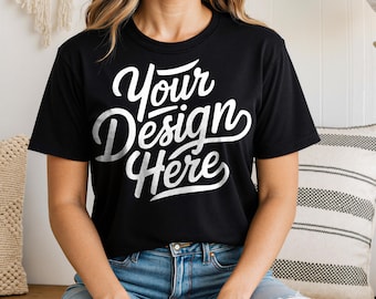 May include: Black crew neck t-shirt with the text "Your Design Here" in white script. The shirt is paired with blue denim jeans. The overall look is casual and comfortable.