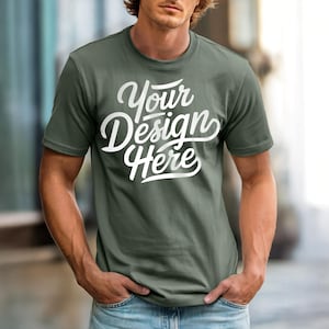May include: Olive green crew neck t-shirt with the text "Your Design Here" in white script. The shirt is made of a soft material and is being worn with blue jeans.