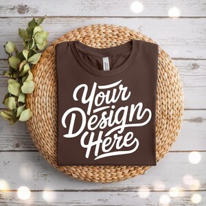 Może przedstawiać: Brązowa koszulka z nadrukiem "Your Design Here" w kolorze białym na tle plecionego wiklinowego.