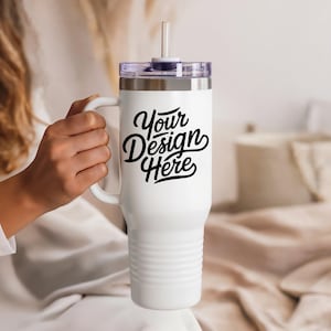 May include: White insulated tumbler with a handle and a clear lid. The tumbler has a black text that says "Your Design Here". A clear straw is inserted into the lid. The tumbler is designed to keep drinks cold or hot.