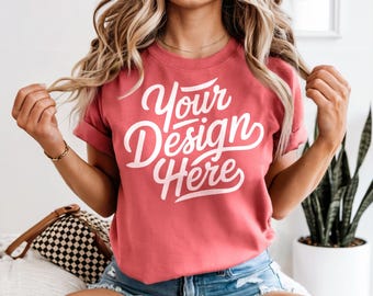 May include: A woman wearing a coral colored t-shirt with the text "Your Design Here" in white. She is wearing blue denim shorts and has long blonde hair.