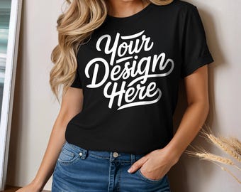 May include: Black crew neck t-shirt with the text "Your Design Here" in white script. The model is wearing blue jeans. The shirt has rolled-up sleeves.