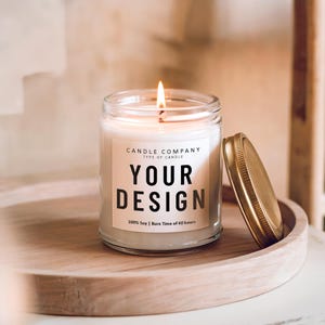 Puede incluir: Un tarro de vela de vidrio transparente con tapa dorada. La vela es blanca y tiene una etiqueta que dice "CANDLE COMPANY TYPE OF CANDLE YOUR DESIGN 100% Soy | Burn Time of 40 hours".