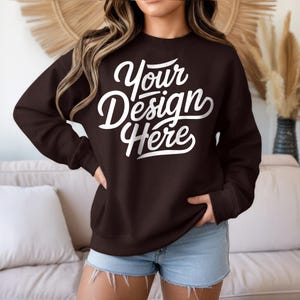 May include: A dark brown sweatshirt with the text "Your Design Here" in a white, cursive font. The sweatshirt is a crew neck style and is being worn with denim shorts. The image is a product mockup.
