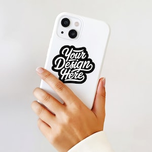 May include: A white smartphone with a black and white sticker that says "Your Design Here" in a cursive font. The phone is held in a person's hand against a white background.