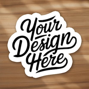May include: A white sticker with the words "Your Design Here" in black, stylized script. The sticker has a unique, irregular shape and is set against a wooden background.