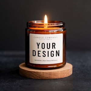 Puede incluir: Una vela encendida en un tarro de vidrio marrón con una etiqueta blanca que dice "YOUR DESIGN". La vela está sobre un pequeño posavasos redondo de madera. También se ve el texto "CANDLE COMPANY" y "Net Wt 8oz | Burn Time of 40 hours".