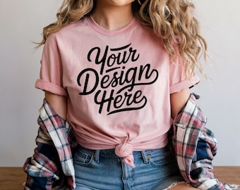 May include: A pale pink t-shirt featuring the text "Your Design Here" in black script. The shirt is knotted at the waist and worn with denim shorts. A plaid shirt is draped over the shoulders.